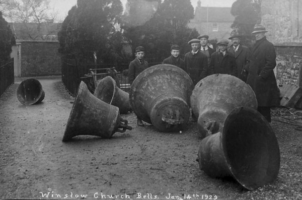 Six bells lying on the ground next to the church with a group of men and boys